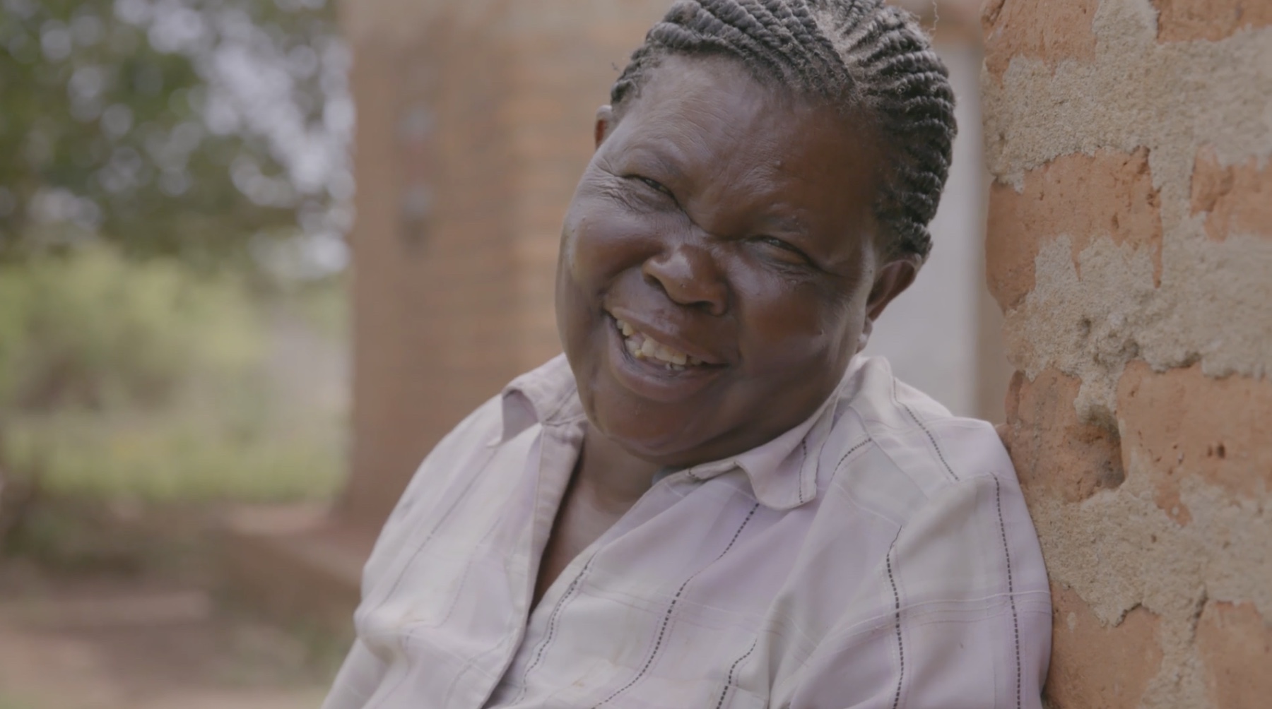 A farmer in Uganda laughing outside her home